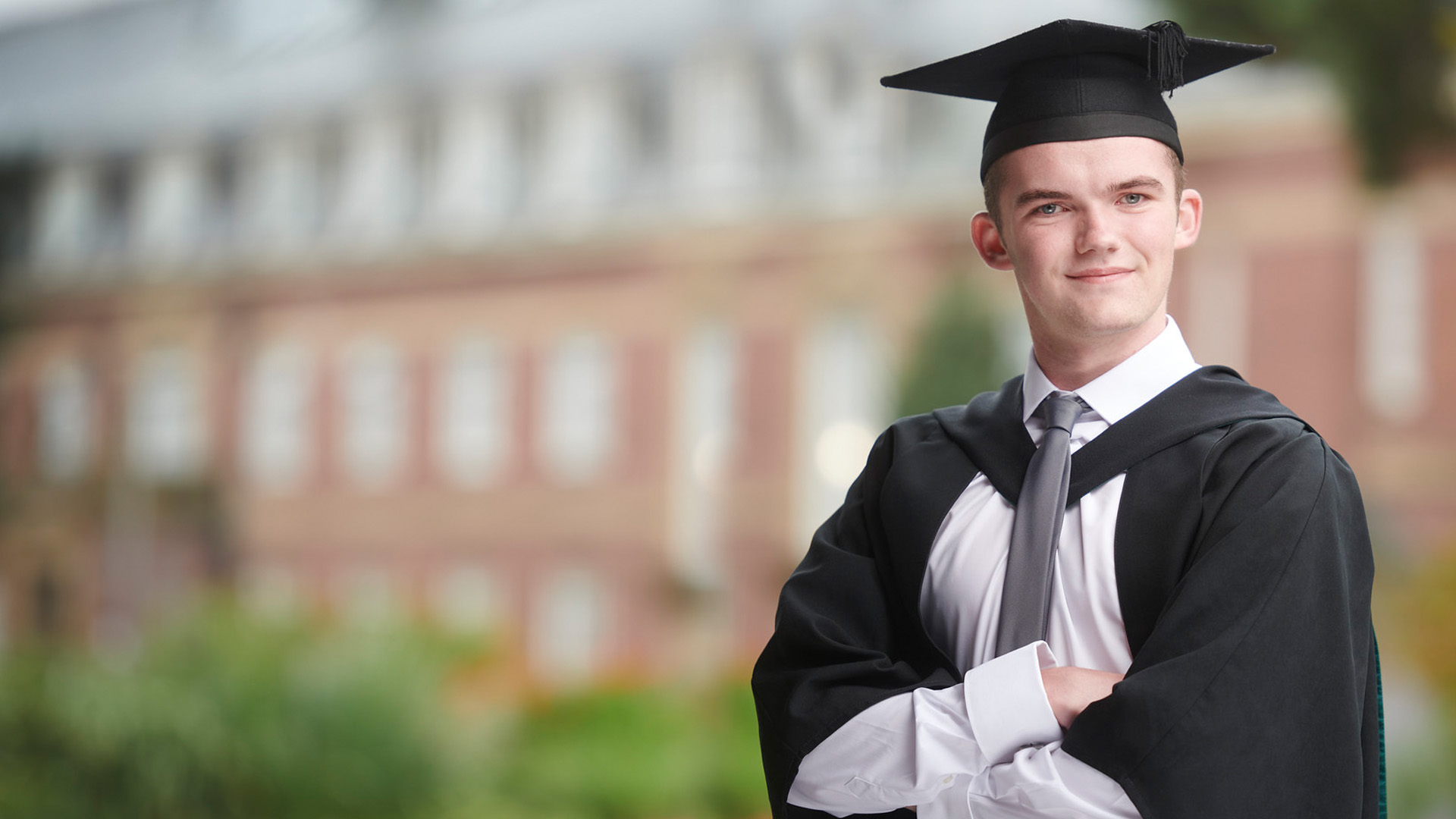 joseph green wearing a cap and gown and smiling with arms folded.