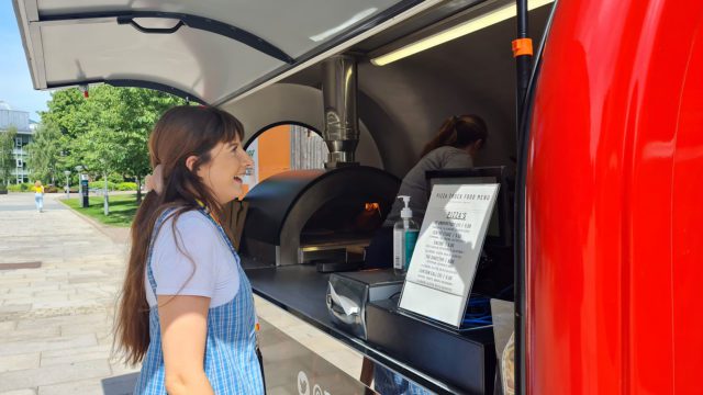 A student waiting for their food at the pizza pop up stall outside of the hub