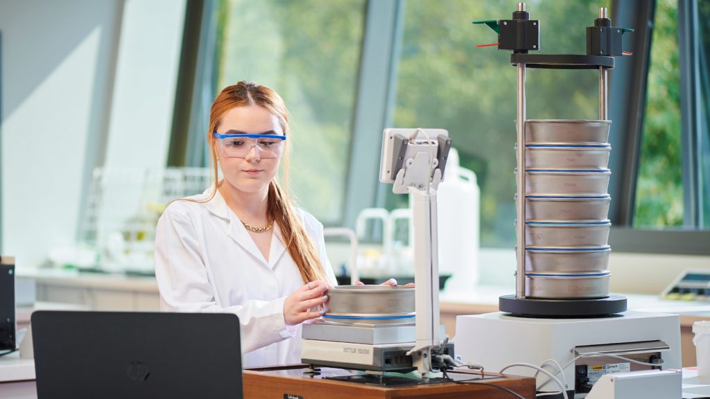 A student wearing lab goggles and looking at a computer