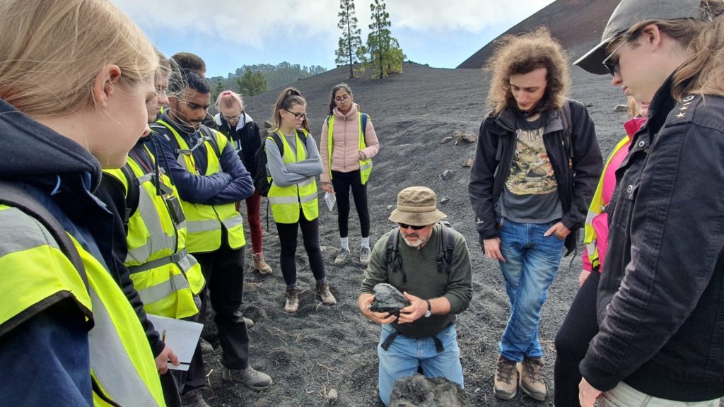 An image of a group of students, and a lecturer who is discussing a rock they are holding. 