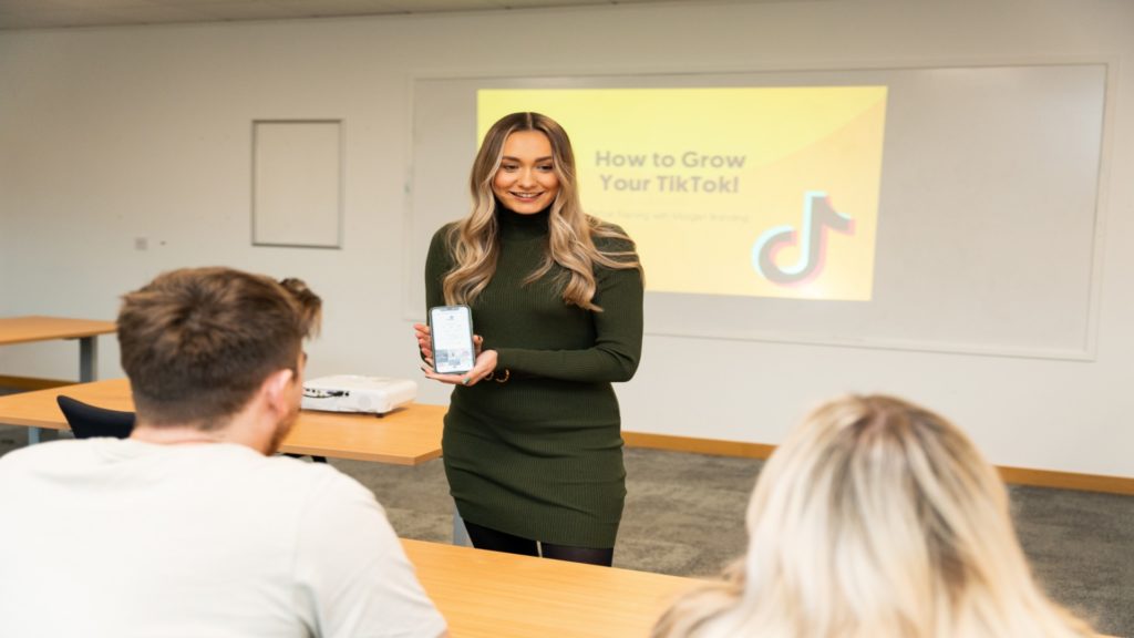 Third year Marketing student showing mobile phone to a class of students