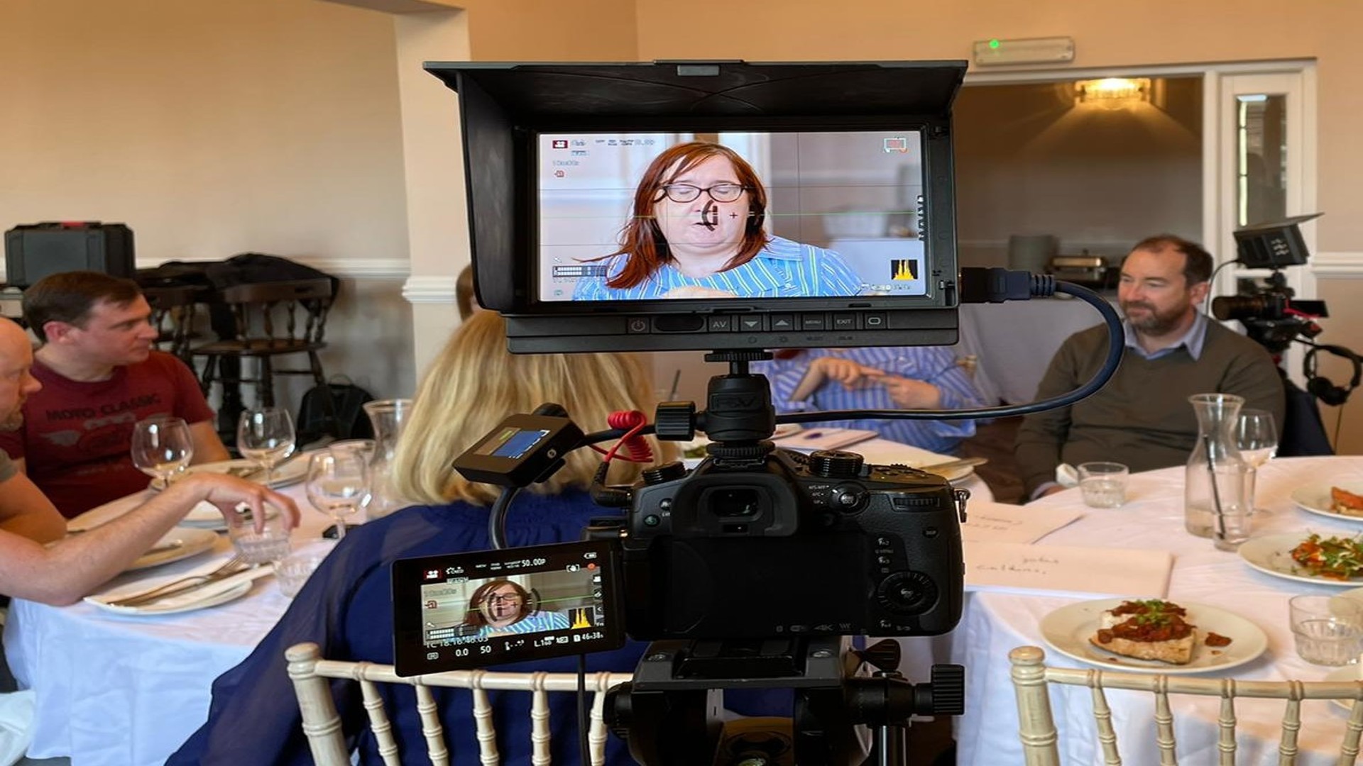 Group of people around a dinner table being filmed for TV.