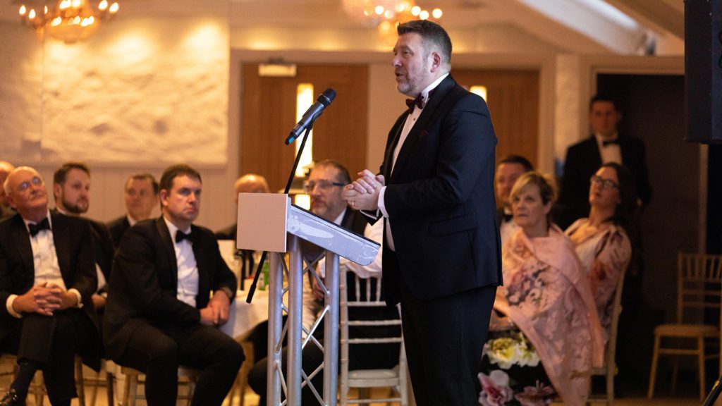 PIc awards night image of man stood on stage giving a speech in black tie dress