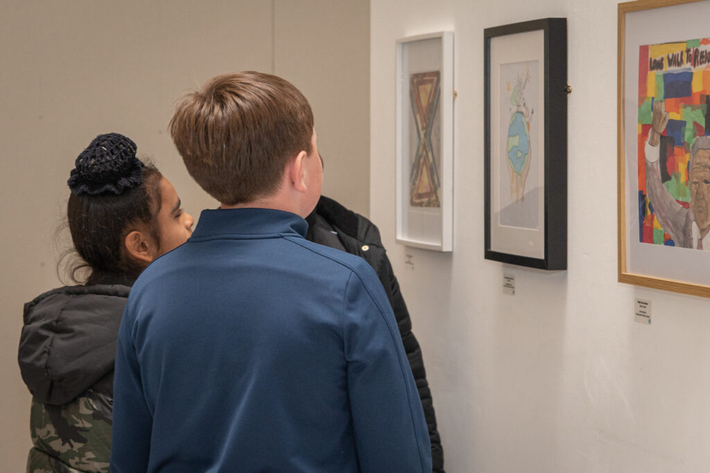 A picture of three children looking at framed artworks on a wall. 