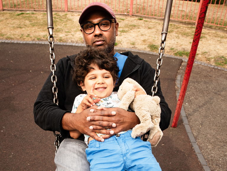 Father sat on a swing with his child. The child is smiling and holding a stuffed animal toy.