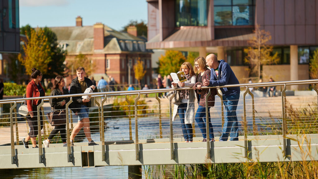 Two parents stand on a bridge with a prospective student reading an open day brochure