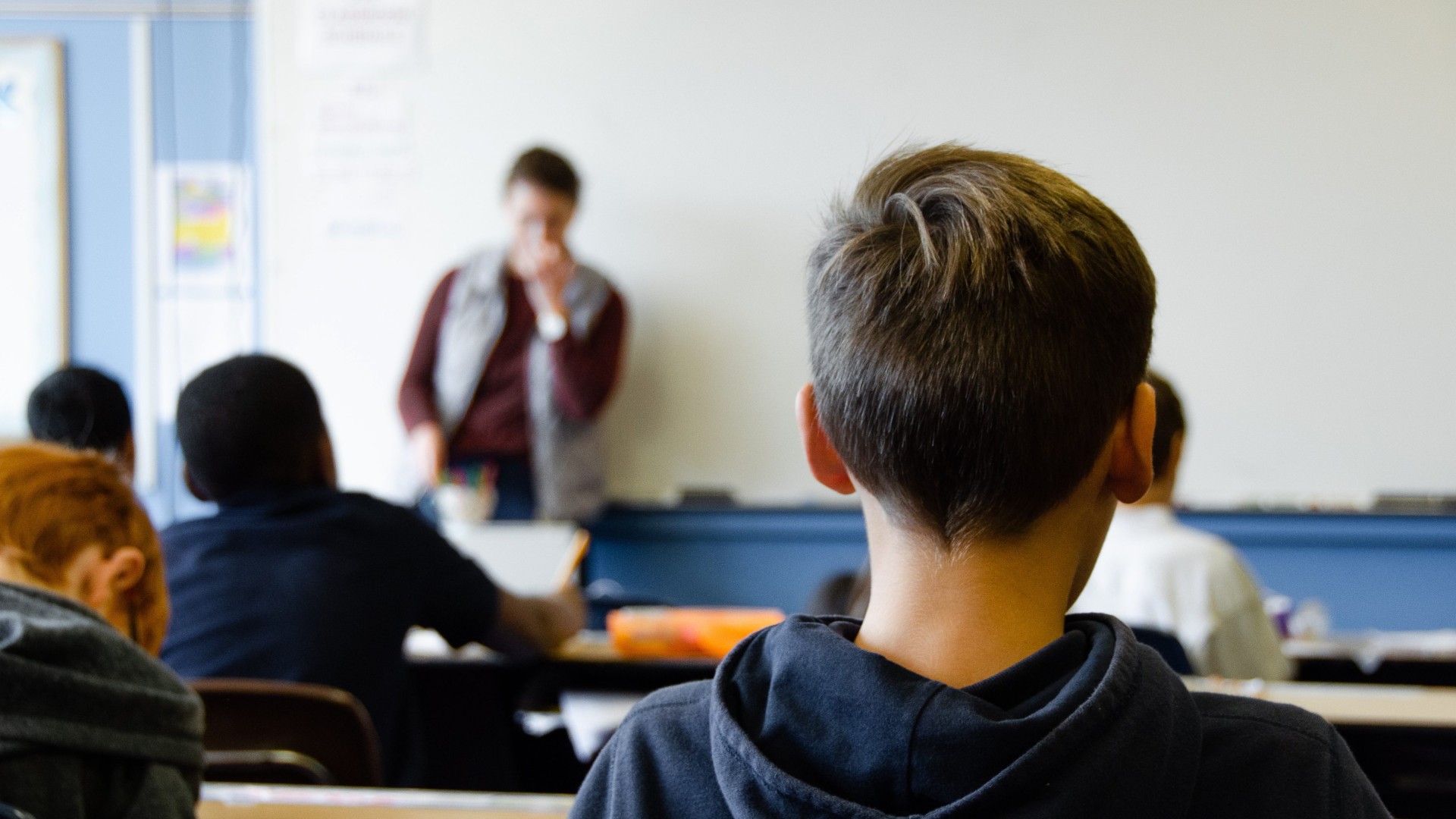 An image of students sat in a classroom. There is a teacher at the front of the room.