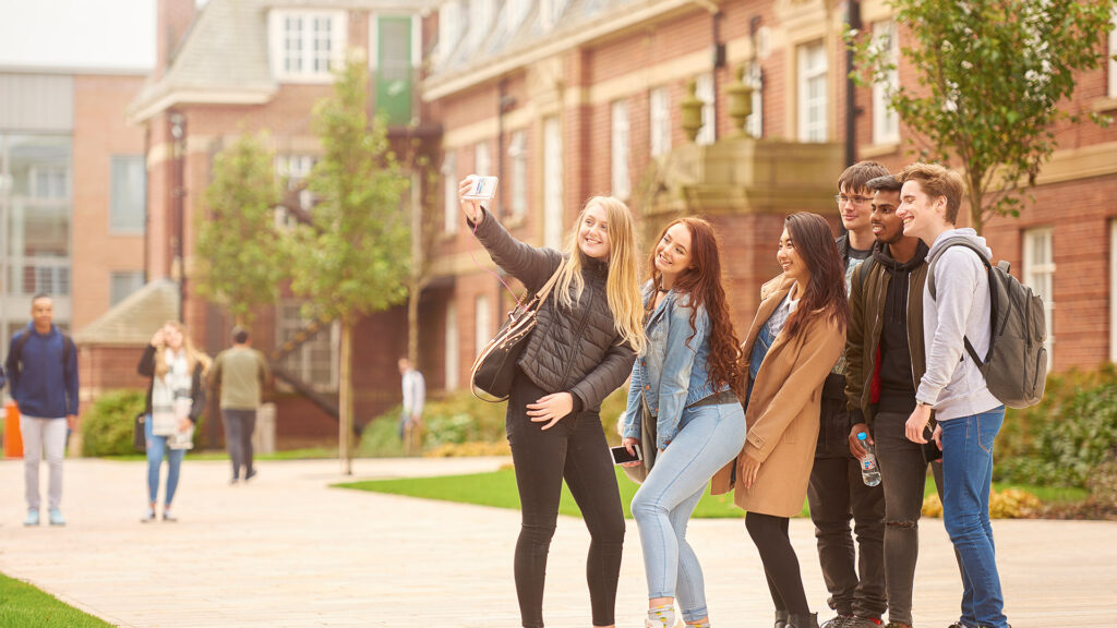a group of students smile for a selfie while stood on campus