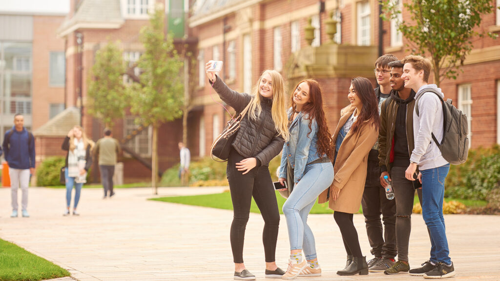 a group of students smile for a selfie while stood on campus