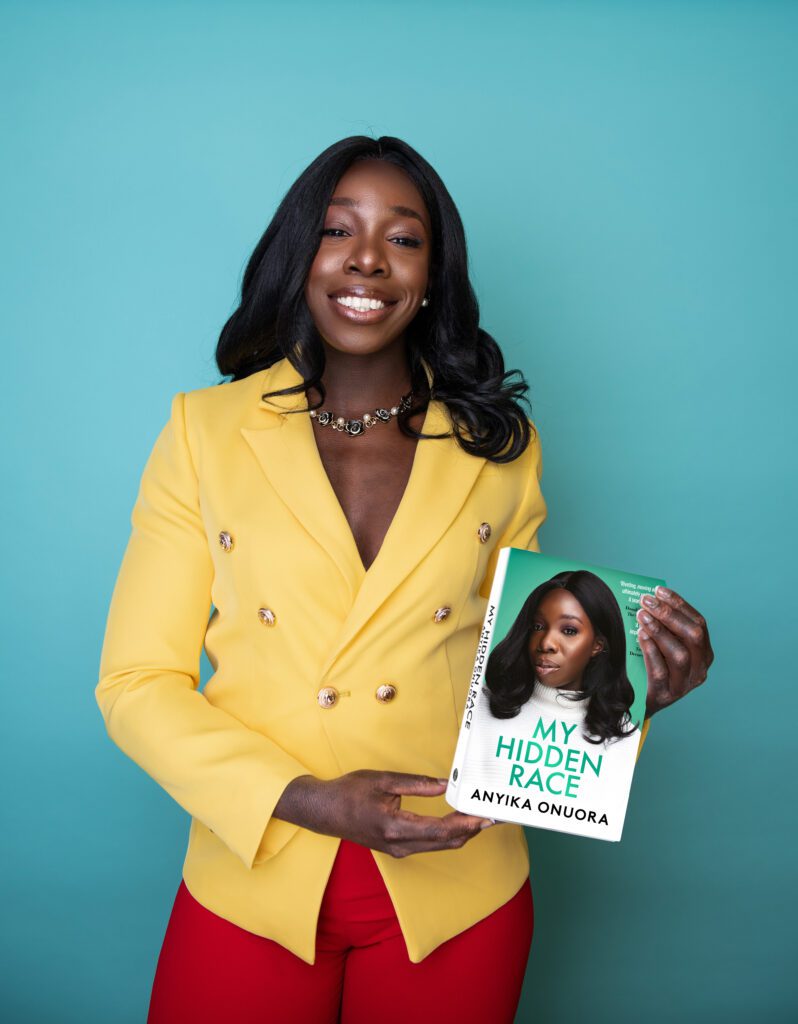 Anyika Onuora holds a copy of her book and smiles at the camera.