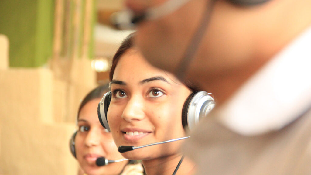 A call operator with their headset on whilst smiling. There are two other call operators sat either side of them with their headsets on.