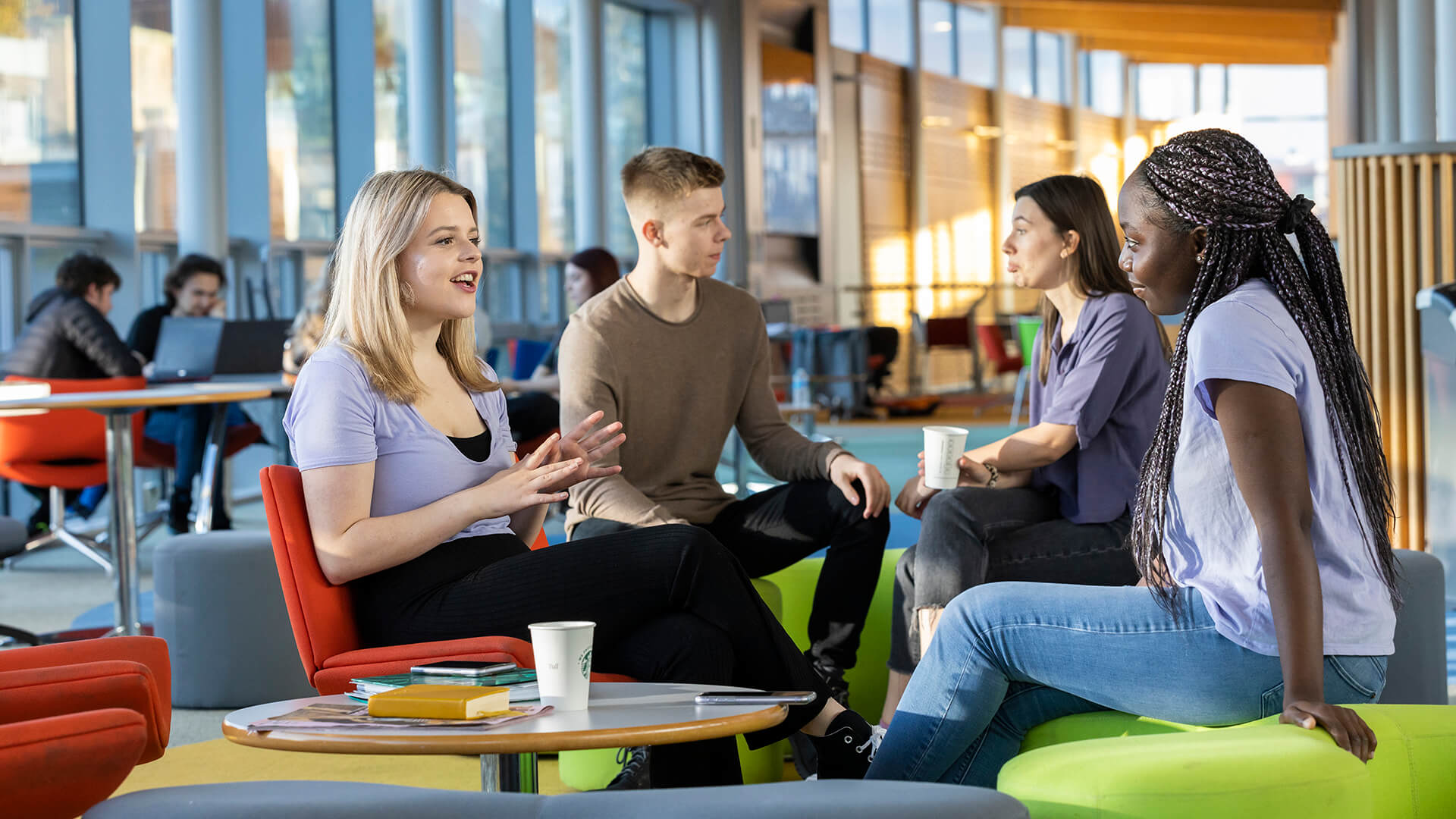 Four students sit together round a small table in the Hub and discuss their studies.