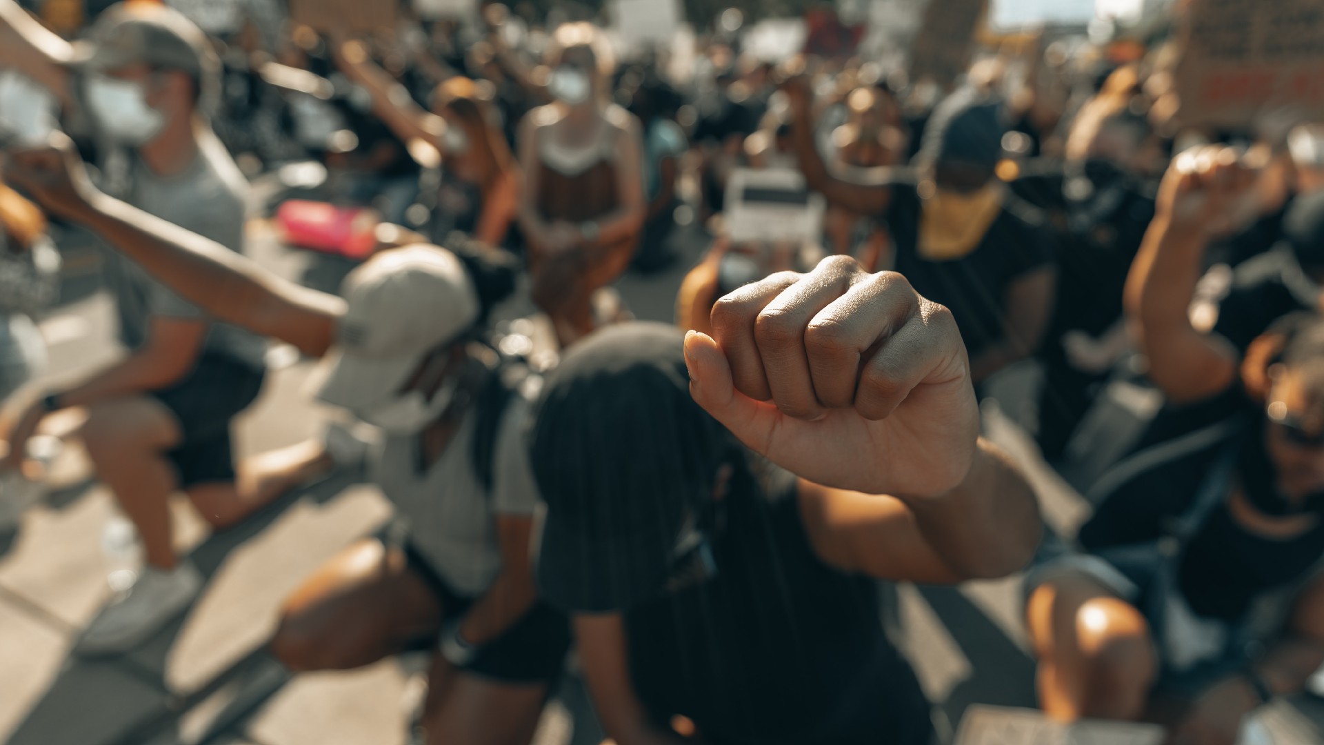 A crowd of people kneel in solidarity with their fists held up in the air.