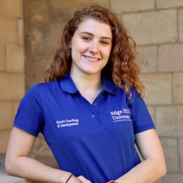 Sport, Physical Activity and Mental Health student, Sophie Warden. Sophie is wearing a blue Edge Hill polo, with 'Sports Coaching & Development' embroidery and an embroidered Edge Hill logo.