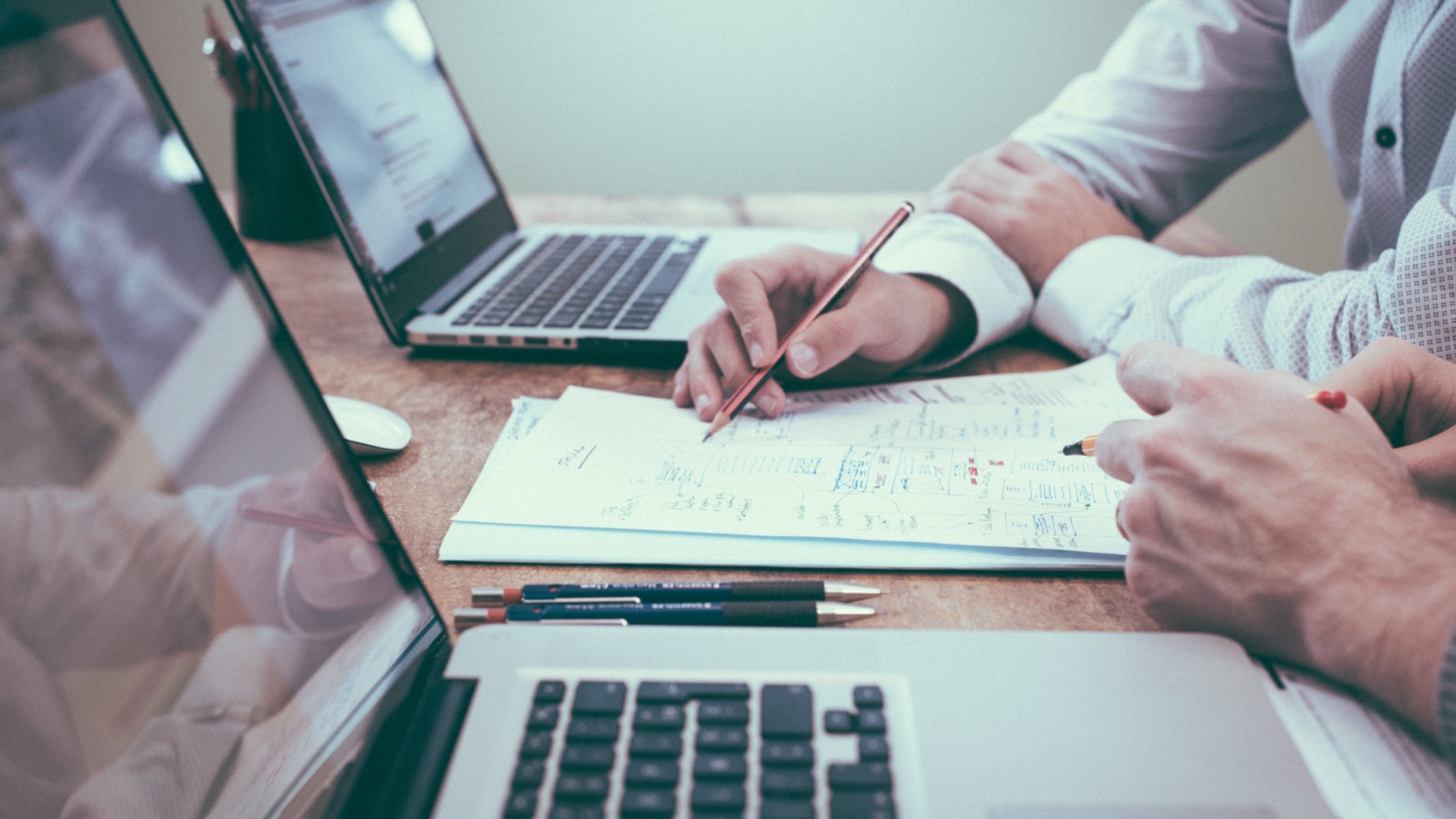 Two people make notes together from their laptops during an accountancy meeting.