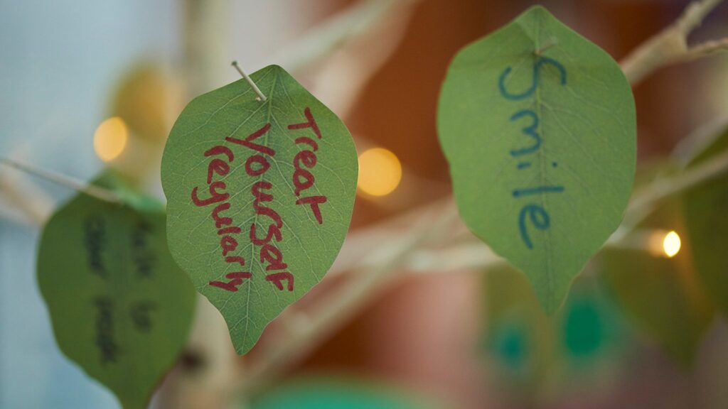 Image of leaves with self-care tips written on them, including 'treat yourself regularly'.