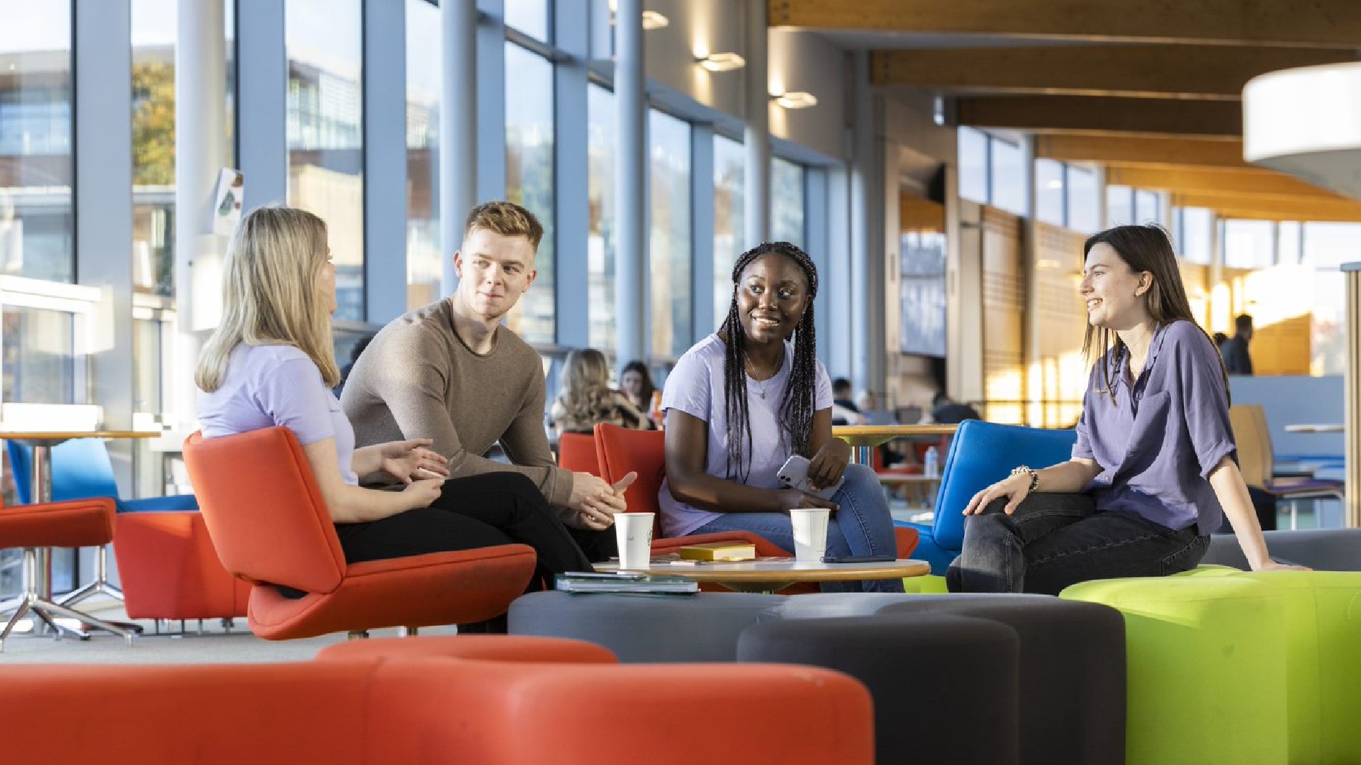 A group of students sit around smiling and talking in the hub