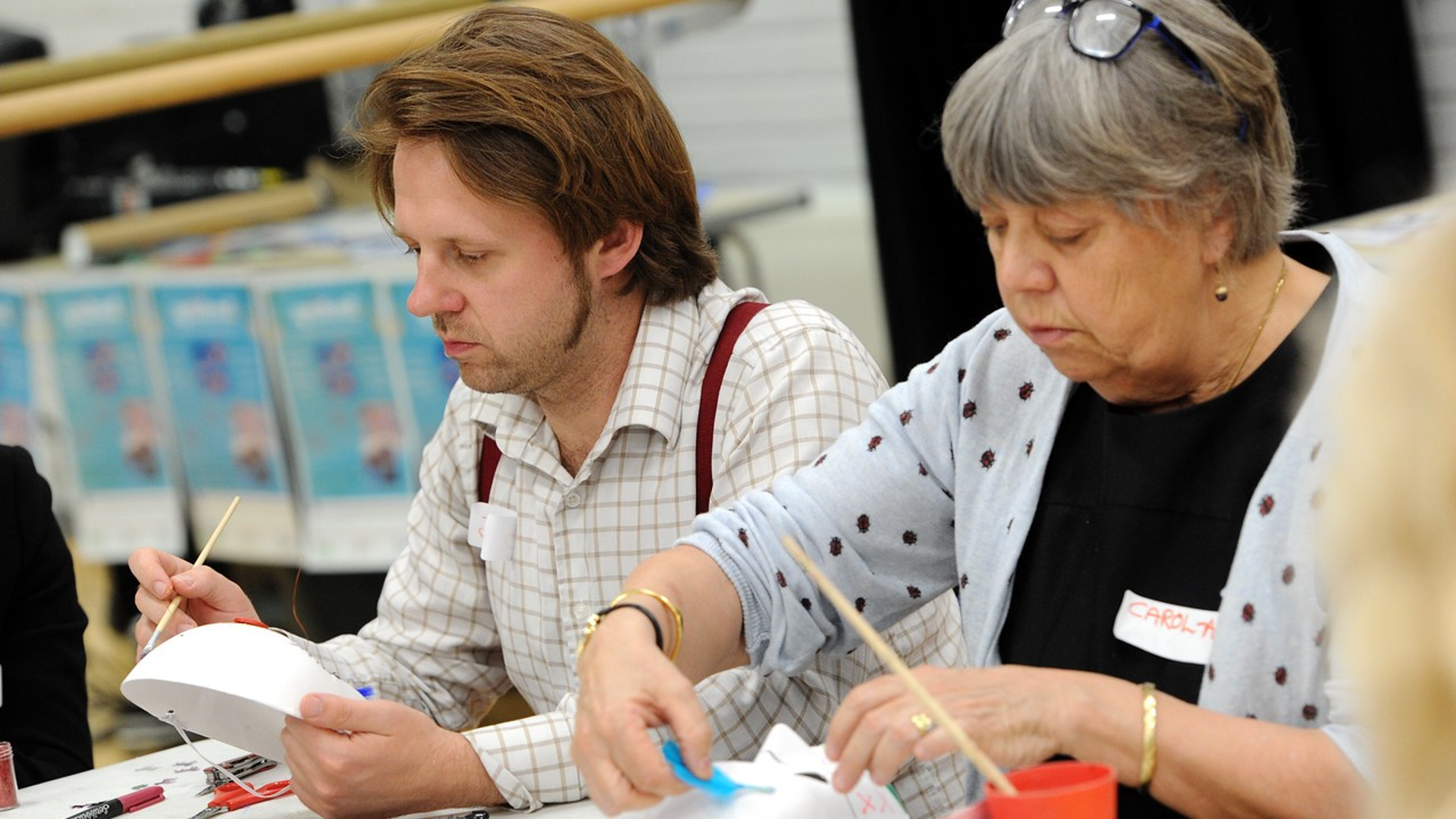 A man and a woman sit next to each other painting masks as part of the Arts for the Blues programme.
