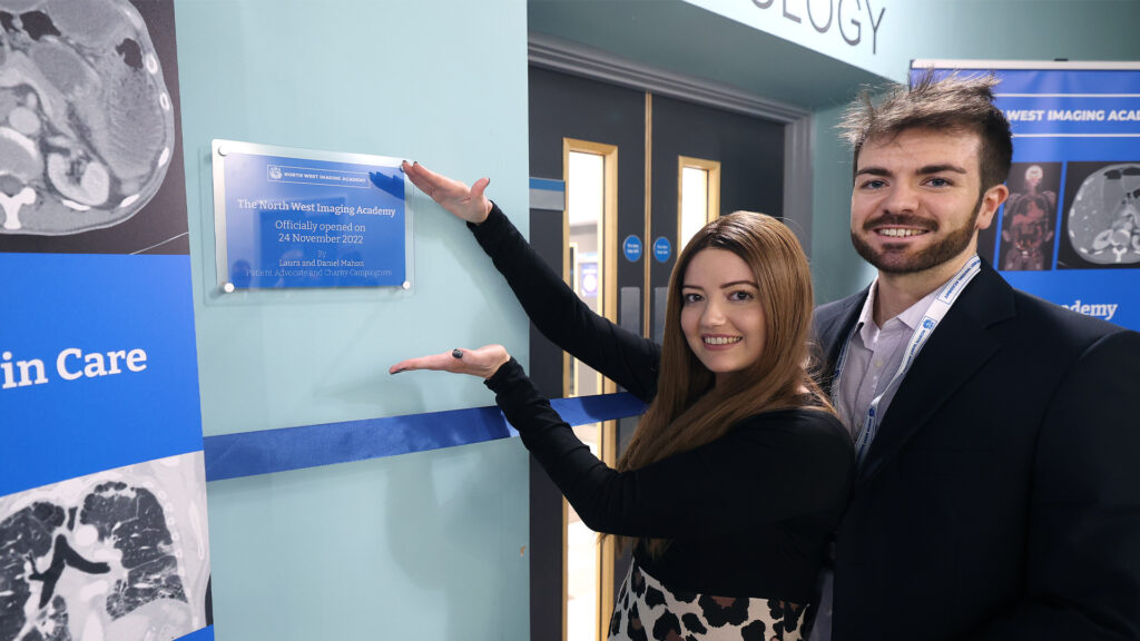 Laura and Daniel stand next to a blue commemorative plaque.