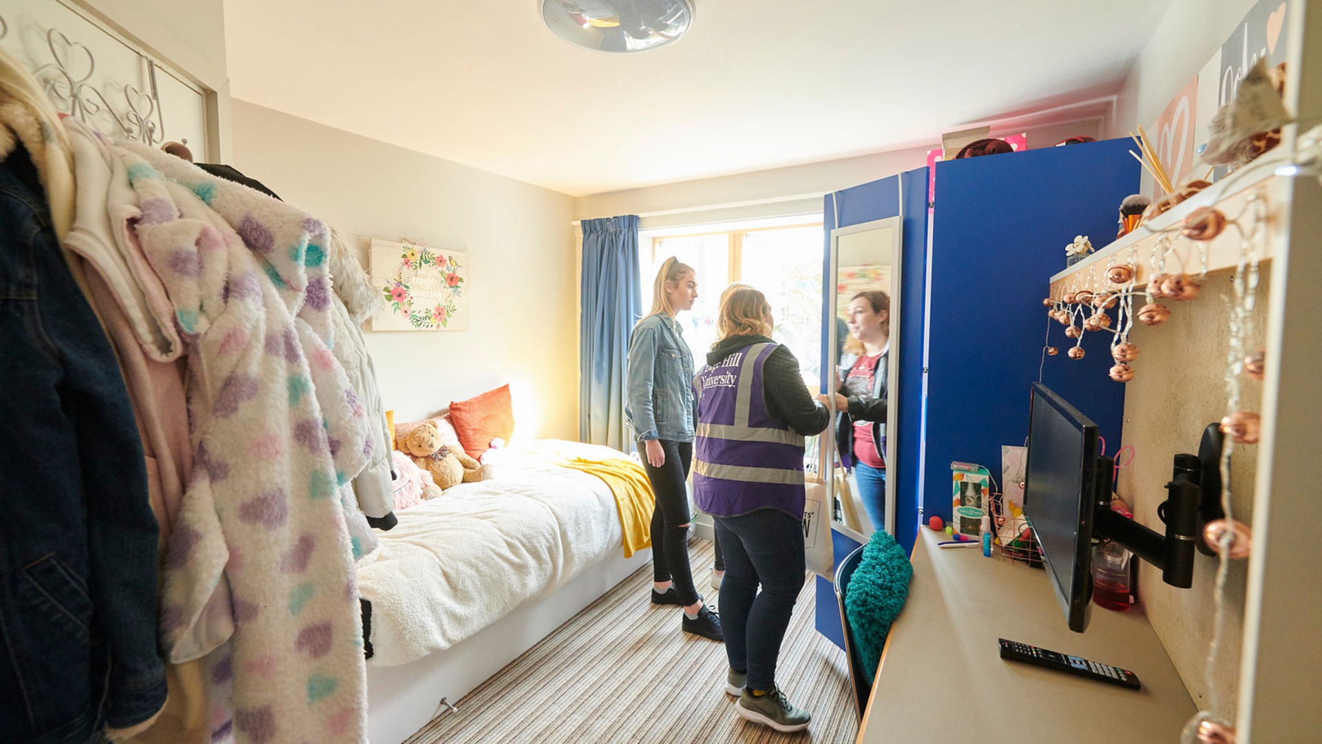 A student guide is giving open day visitors a tour of a students accommodation bedroom.