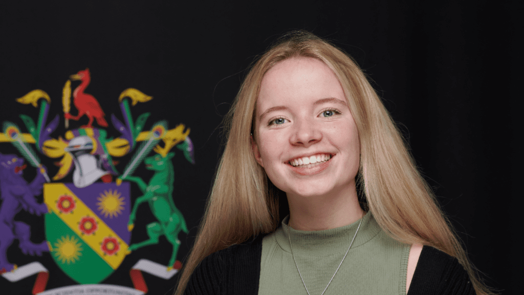 A smiling Charlotte Black next to the Edge Hill University crest