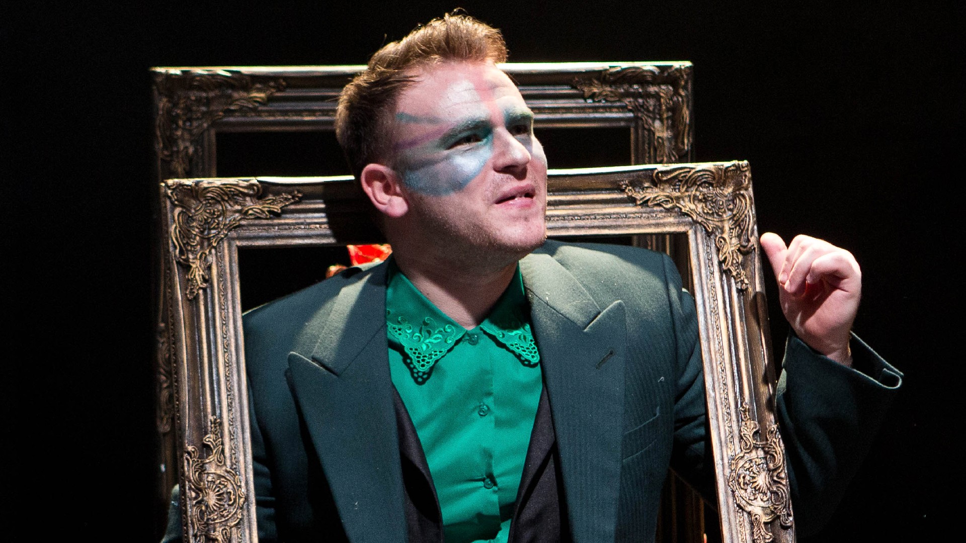 a performer on stage with stage makeup on and stood in a large picture frame