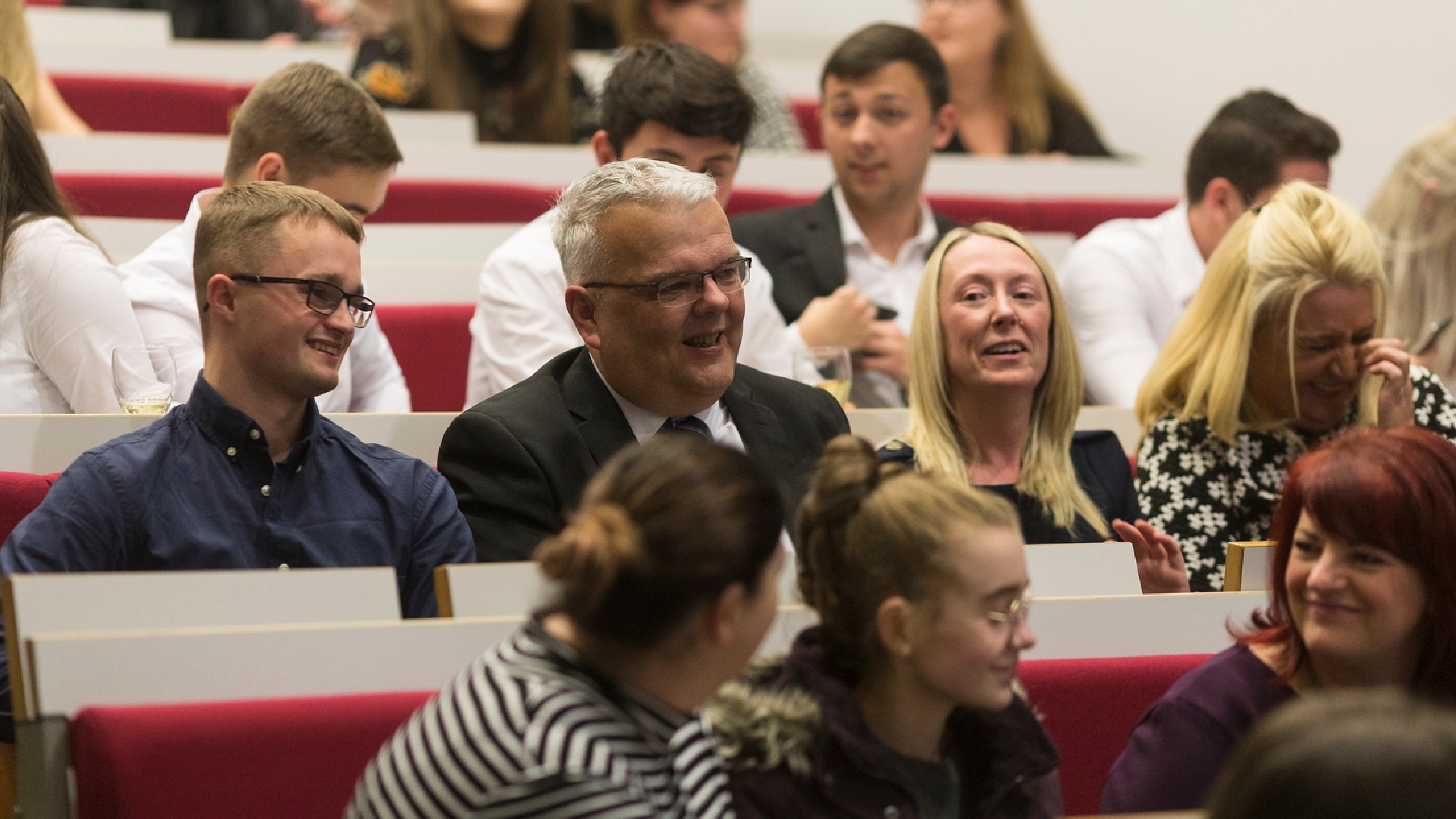 A group of students laugh and smile while seated in row of a lecture theatre