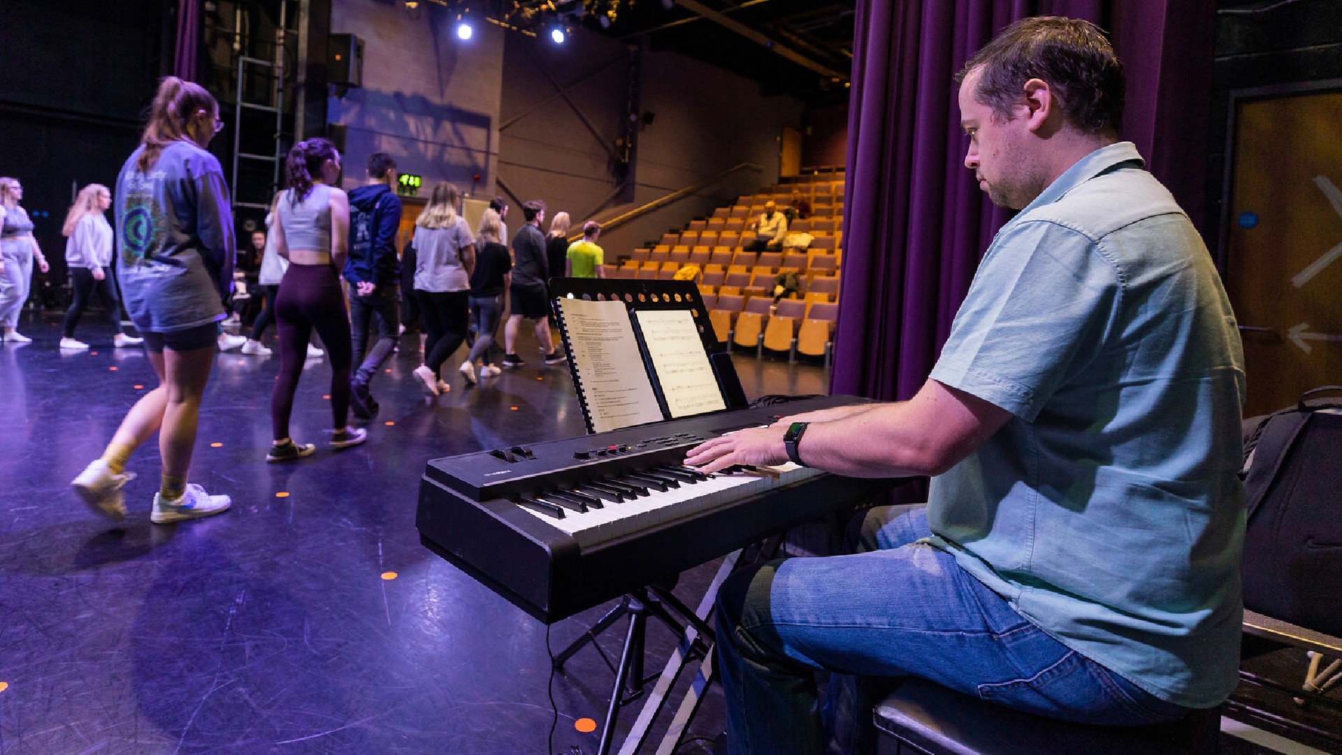 Someone playing keyboard as a rehearsal for a play happens on stage