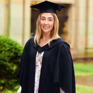 BSc (Hons) Marketing with Digital Communications alumni student, Jessica Barker, wearing a graduation cap an gown outside the Main building.