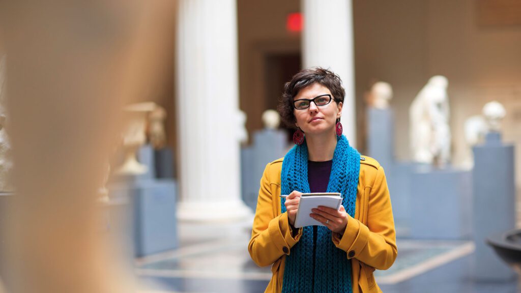 A person is stood in a museum looking at one of the displays. They have a notepad in their hand and are taking notes whilst admiring the museum piece.