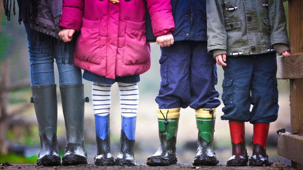Children stand in a line wearing boots covered in mud.