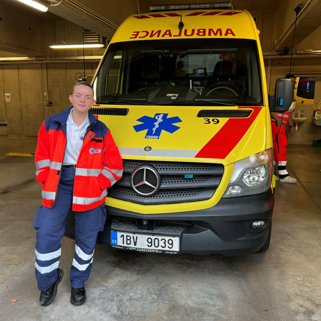 Katie Duxbury wears a paramedic uniform and stands in front of an ambulance.