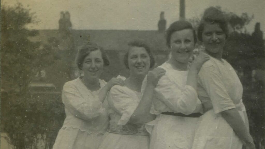A black and white photograph of four women stood in a line smiling at the camera.