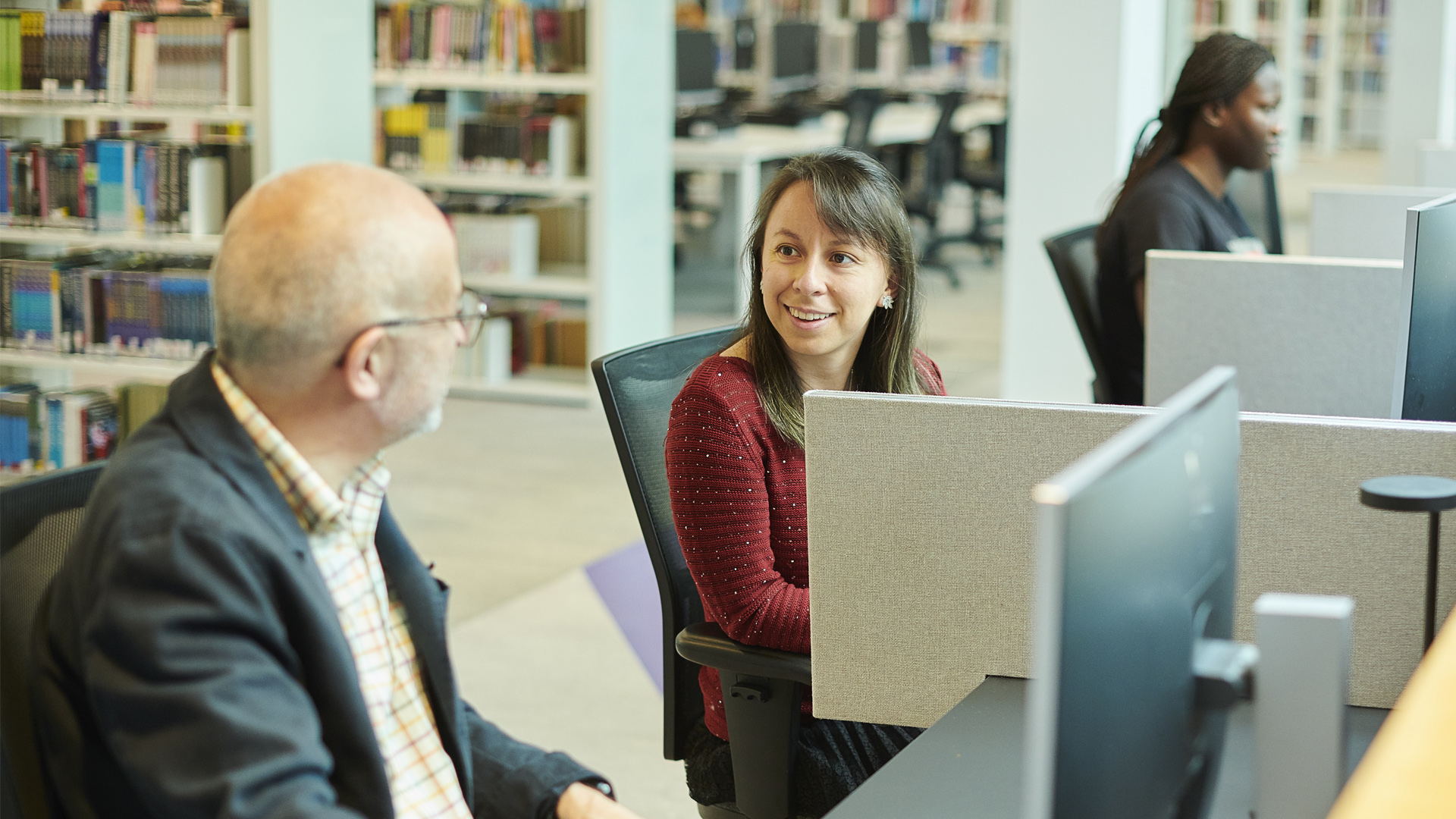 Three students sitting next to each other in Catalyst on computers talking.