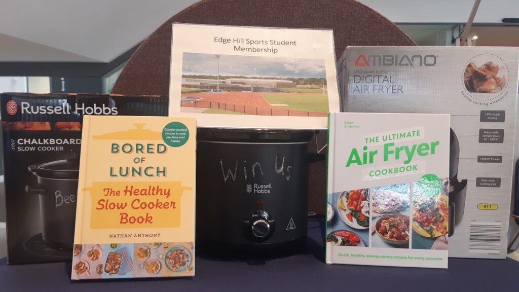 Competition prizes on top of a table. The prizes include a slow cooker, cookbooks, Edge Hill Sports student membership and an air fryer