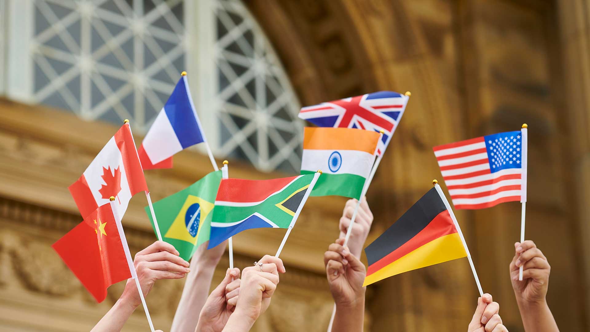 A group of students hands raising small country flags in the air.