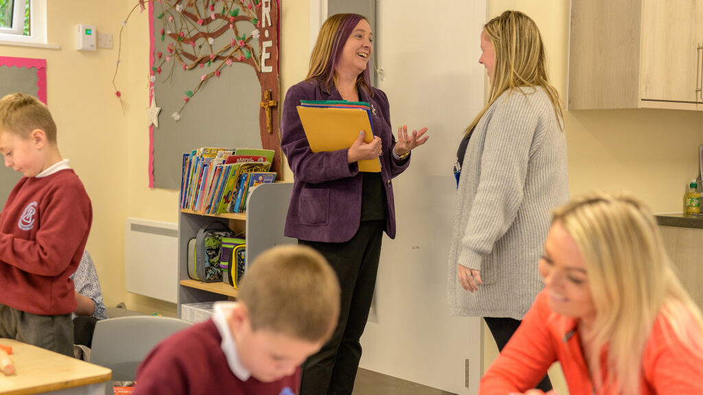 Reachout ASC manager Lynn talks to a teacher in a busy classroom setting