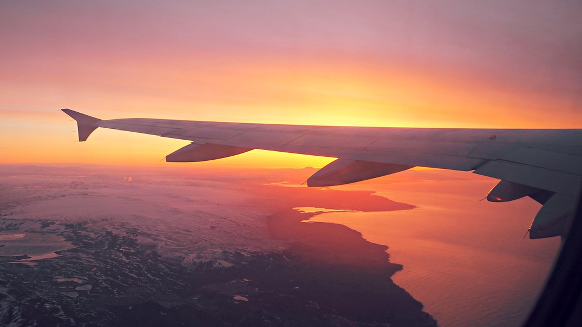 The wing of a plane in flight. The sky is a deep shade of lilac and orange.