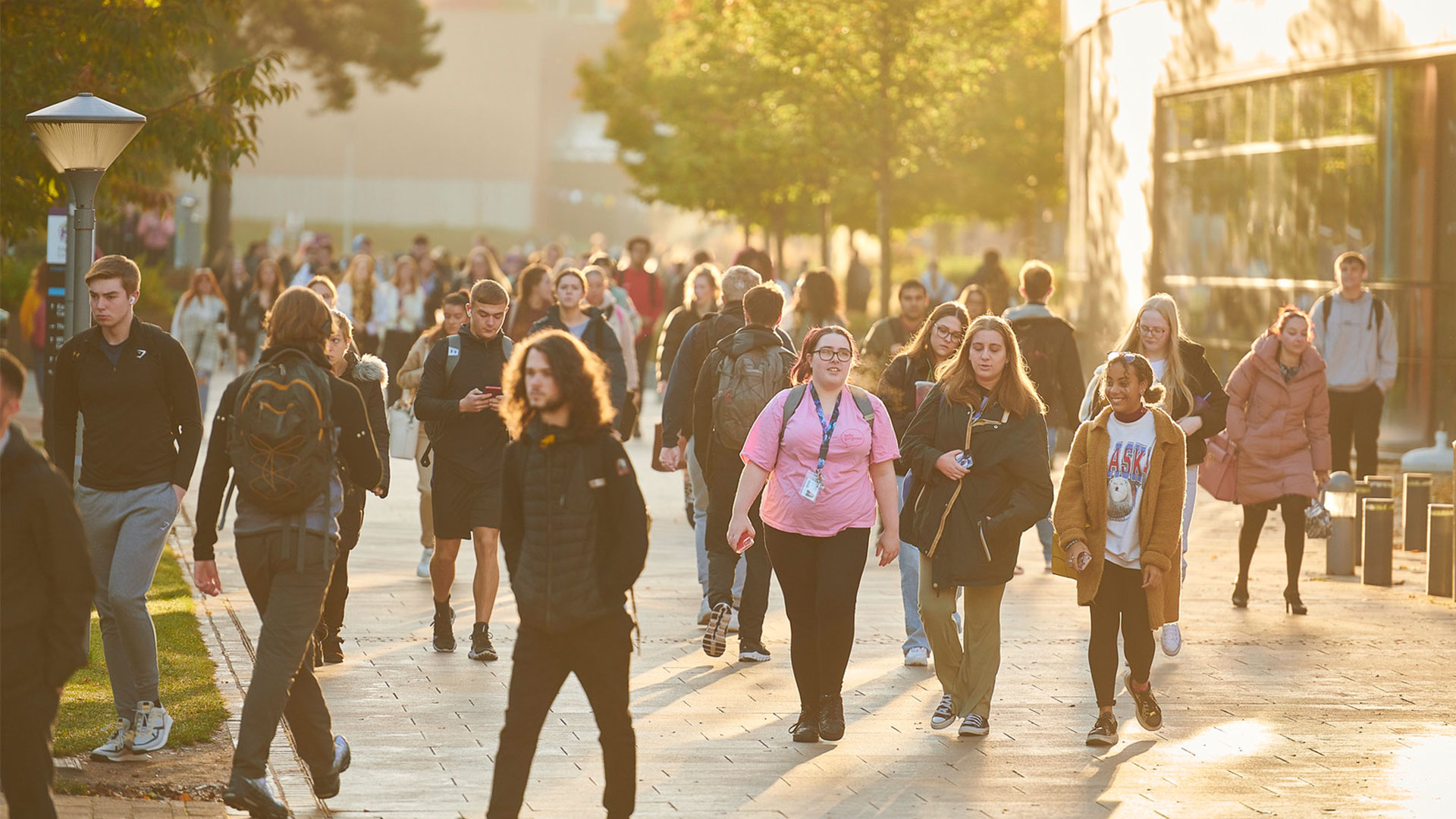 The sun is setting in the background of a busy campus as students walk around in small groups