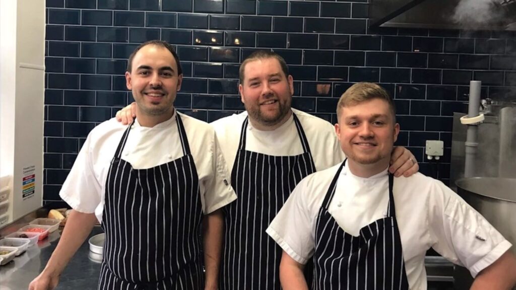 A picture of James with two other chefs in a kitchen.