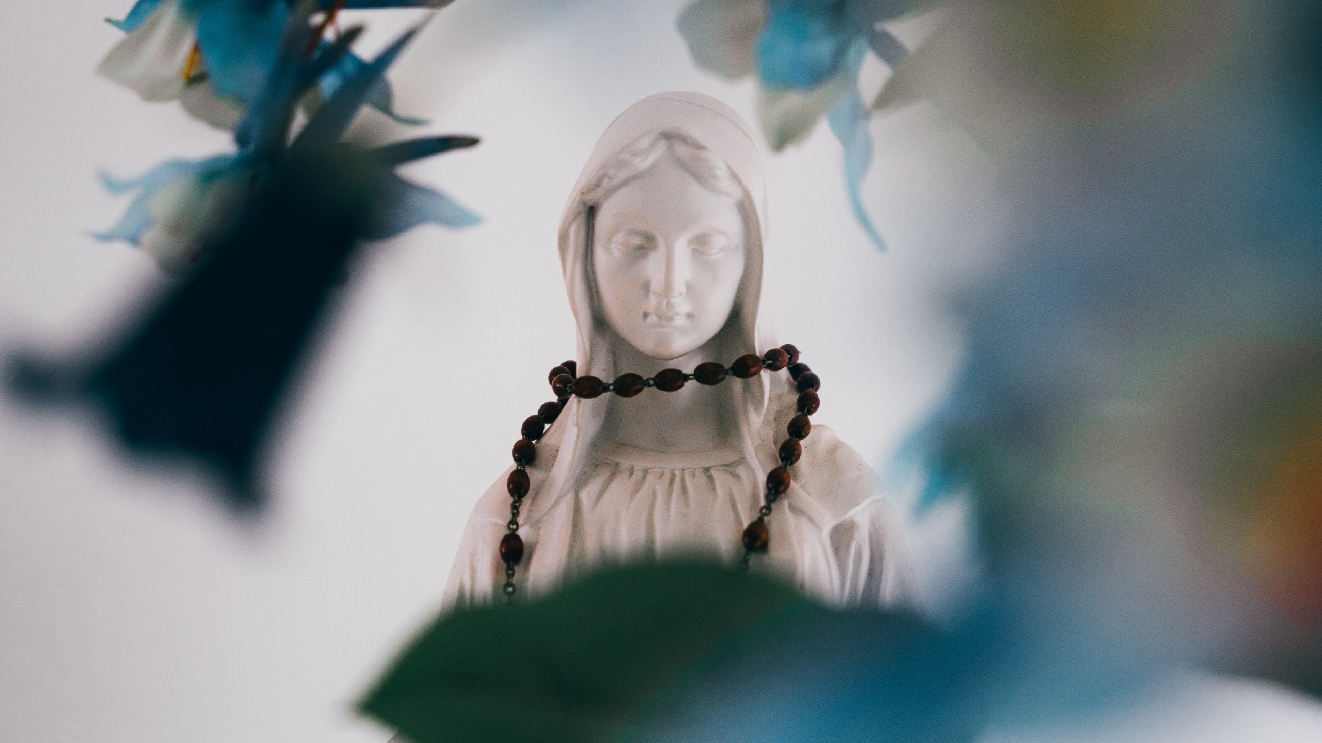 A statue of the Virgin Mary with rosary beads draped around it.