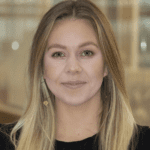 Headshot of Ellie Paulie. She has blonde hair and is smiling to camera.