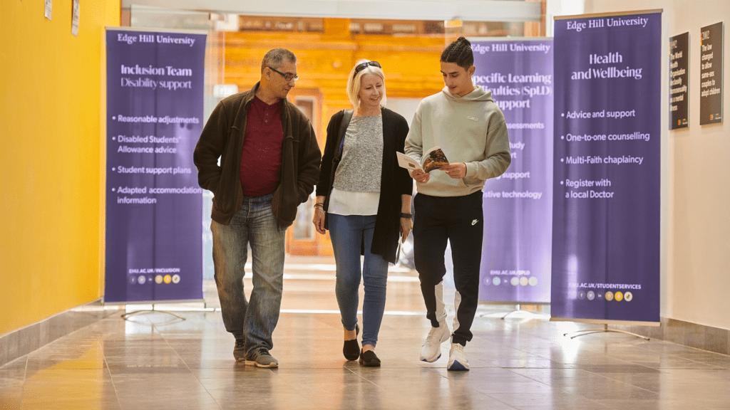 Student and their parents walk through Hale Hall on an open day. Signs advertising Health and Wellbeing and the Inclusion Team can be seen in the background.