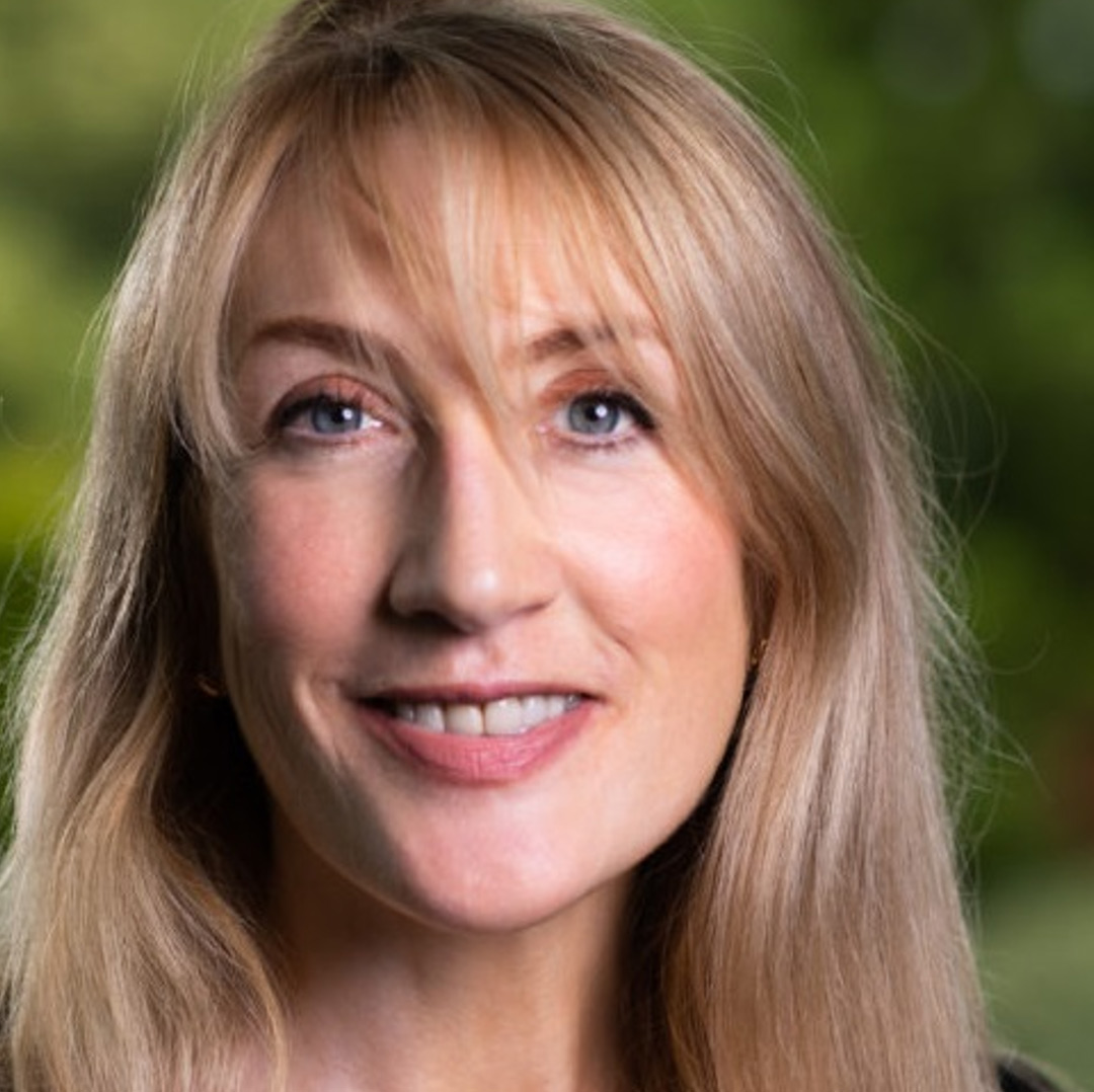 An image of Victoria Foster looking into the camera, there is various greenery in the background.