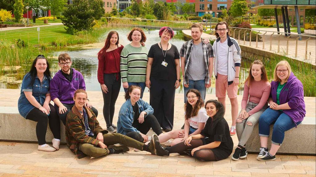 The student drama group, Mrs Pankhursts' Players are sat by the lake on the Edge Hill University campus. 