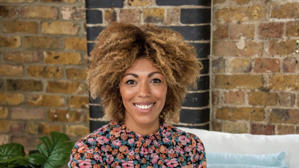 Dr Zoe Williams smiles at the camera while sitting on a sofa.