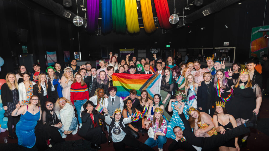 Edge Hill Pride event - Queer Prom 2023. Group of students celebrating a Pride event wearing crowns and holding a flag to represent the queer community. Photo by Student's Union
