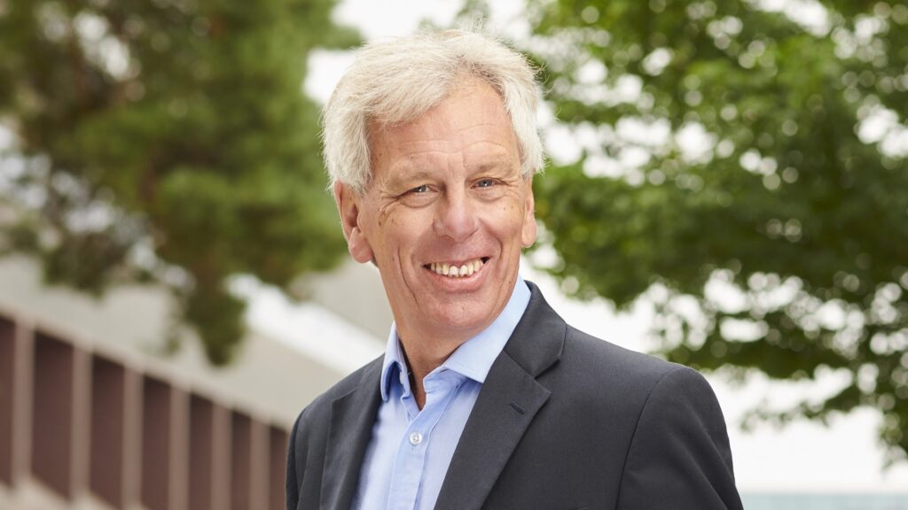 John Cater smiles at the camera with leafy trees in the background.