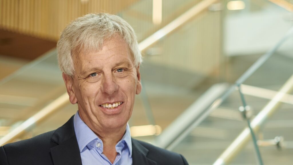 Vice-Chancellor John Cater stands near stairs in the Catalyst and smiles at the camera.