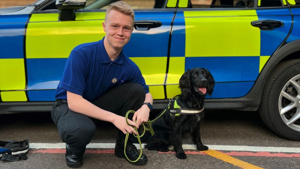 Kien Kirk kneeling down in front of a police car next to a black-haired police dog